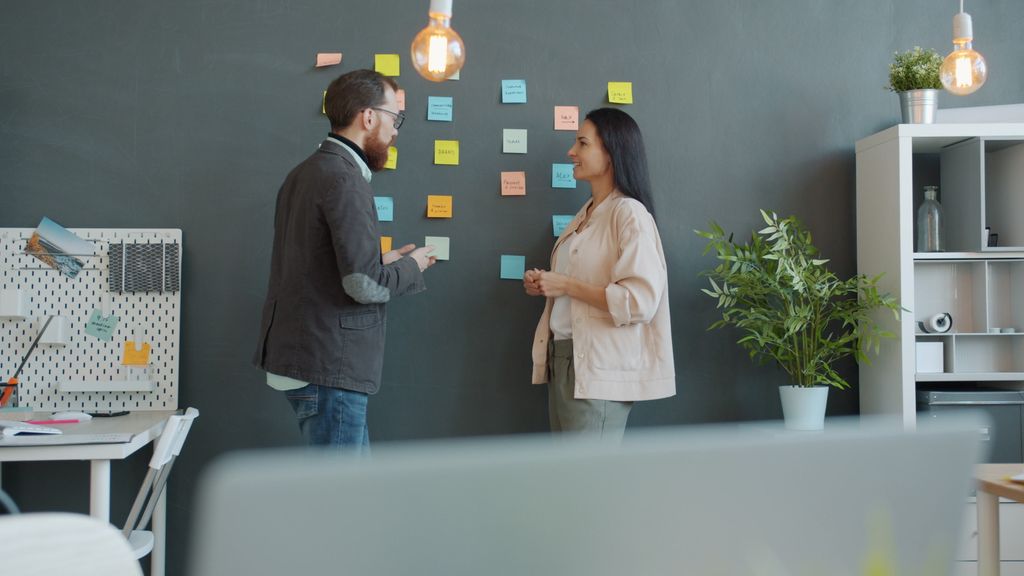 Two colleagues discussing ideas in a modern office using sticky notes on a wall.